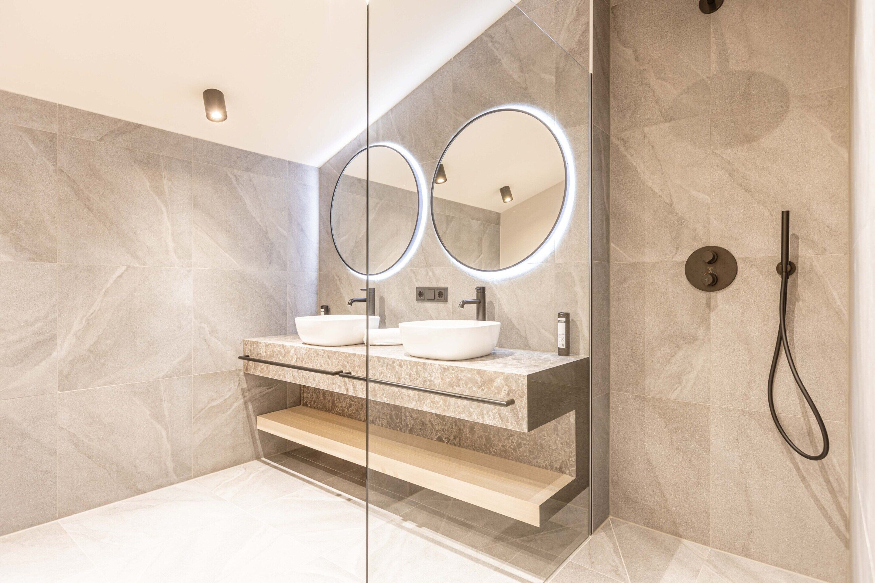 A modern bathroom with two sinks, a glass shower enclosure, and a marble wall.