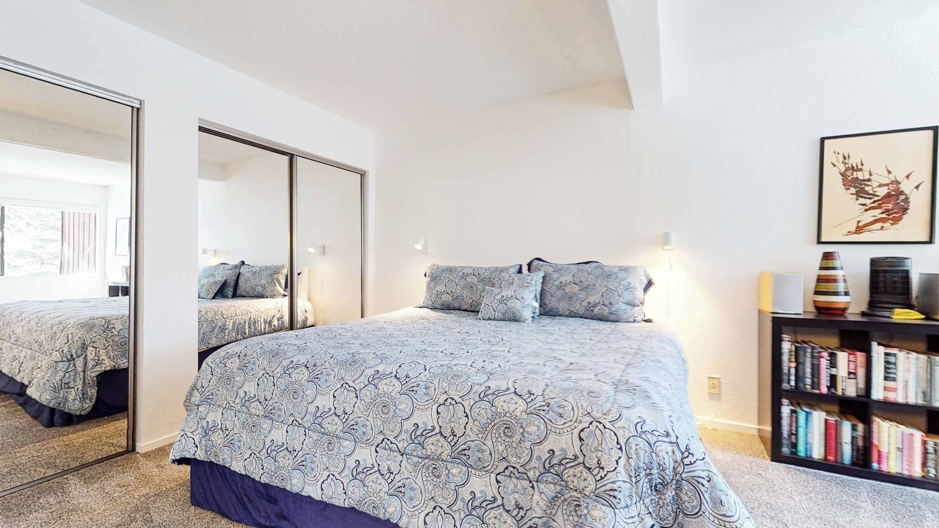 A bedroom with a large bed, a wardrobe, a bookshelf, and a framed picture on the wall.