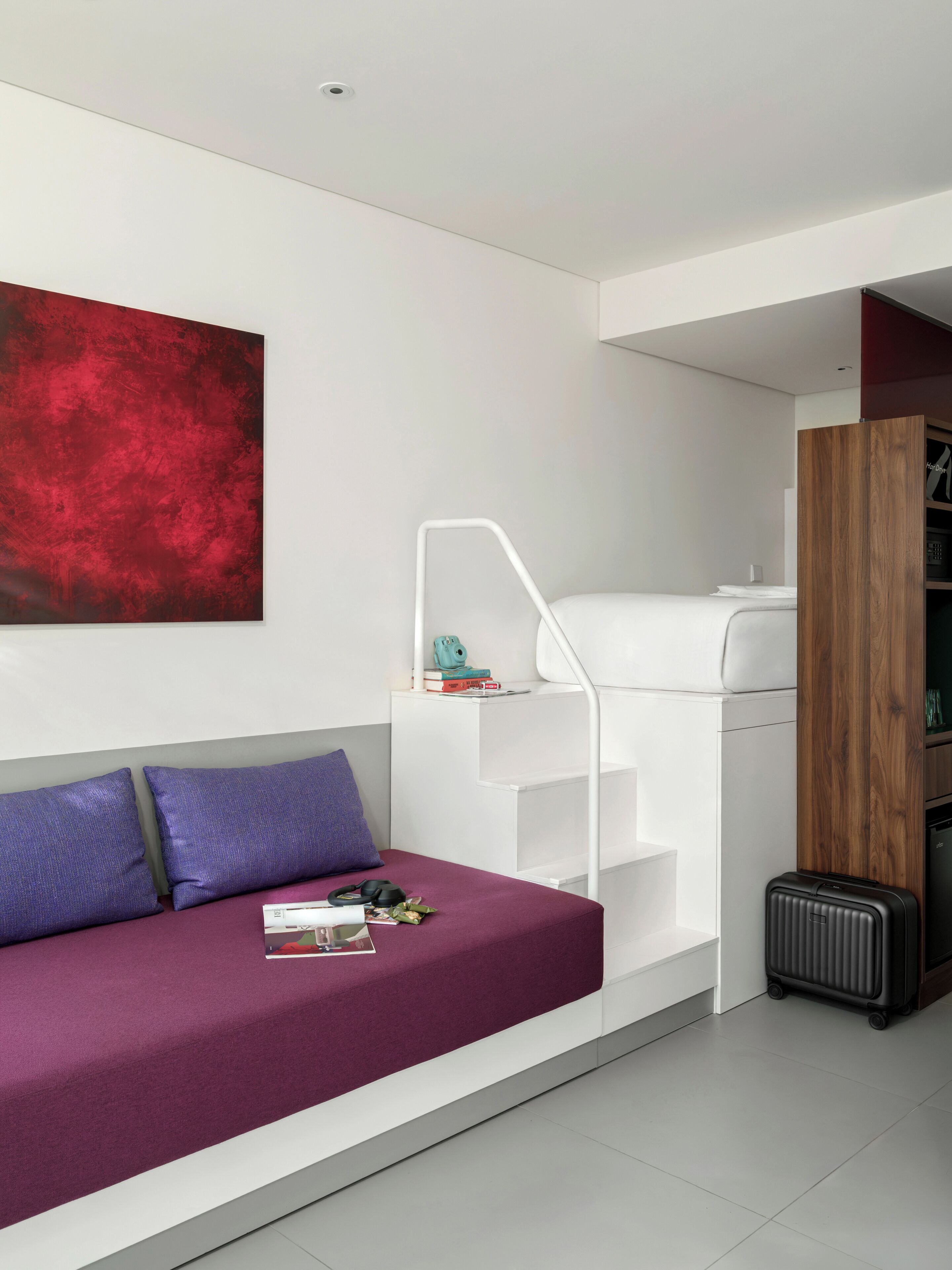 A modern room with a sofa, a red abstract painting, a staircase, a wooden cabinet, and a suitcase.