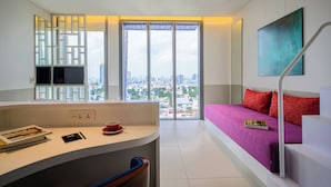 Een moderne hotelkamer met een bureau, een bed met rode kussens, een groot raam met uitzicht over de stad en een trap.
