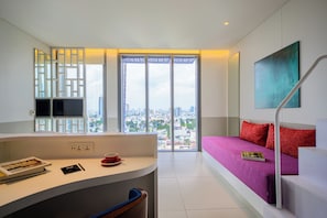 A modern hotel room with a city view, a sofa, a desk with a cup and book, and a staircase. - Wink Hai Phong Centre, Unscripted by Hyatt - 24 Hours stay (Hai Phong)