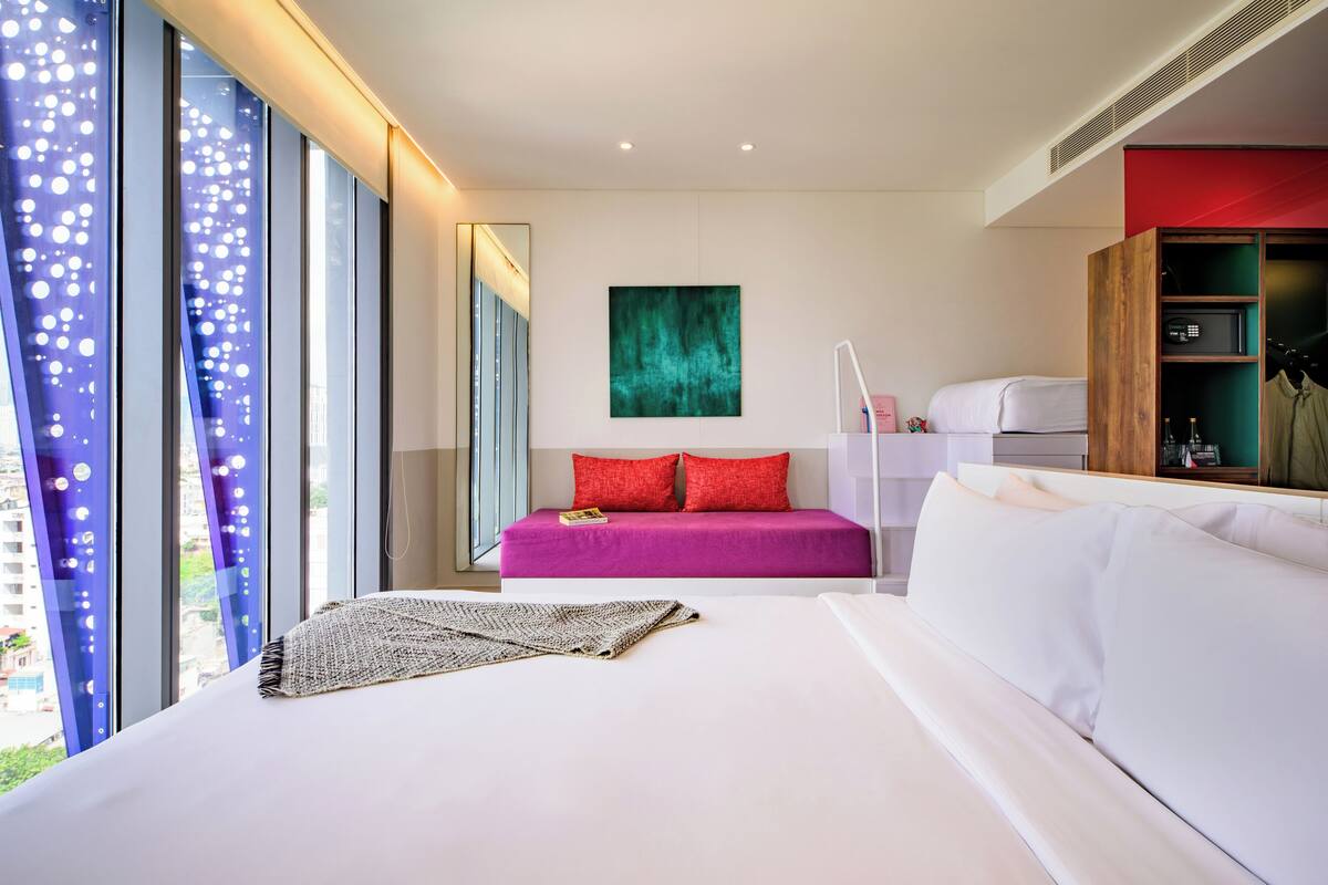Una habitación de hotel moderna con una cama grande, un pequeño sofá, un escritorio y un armario.