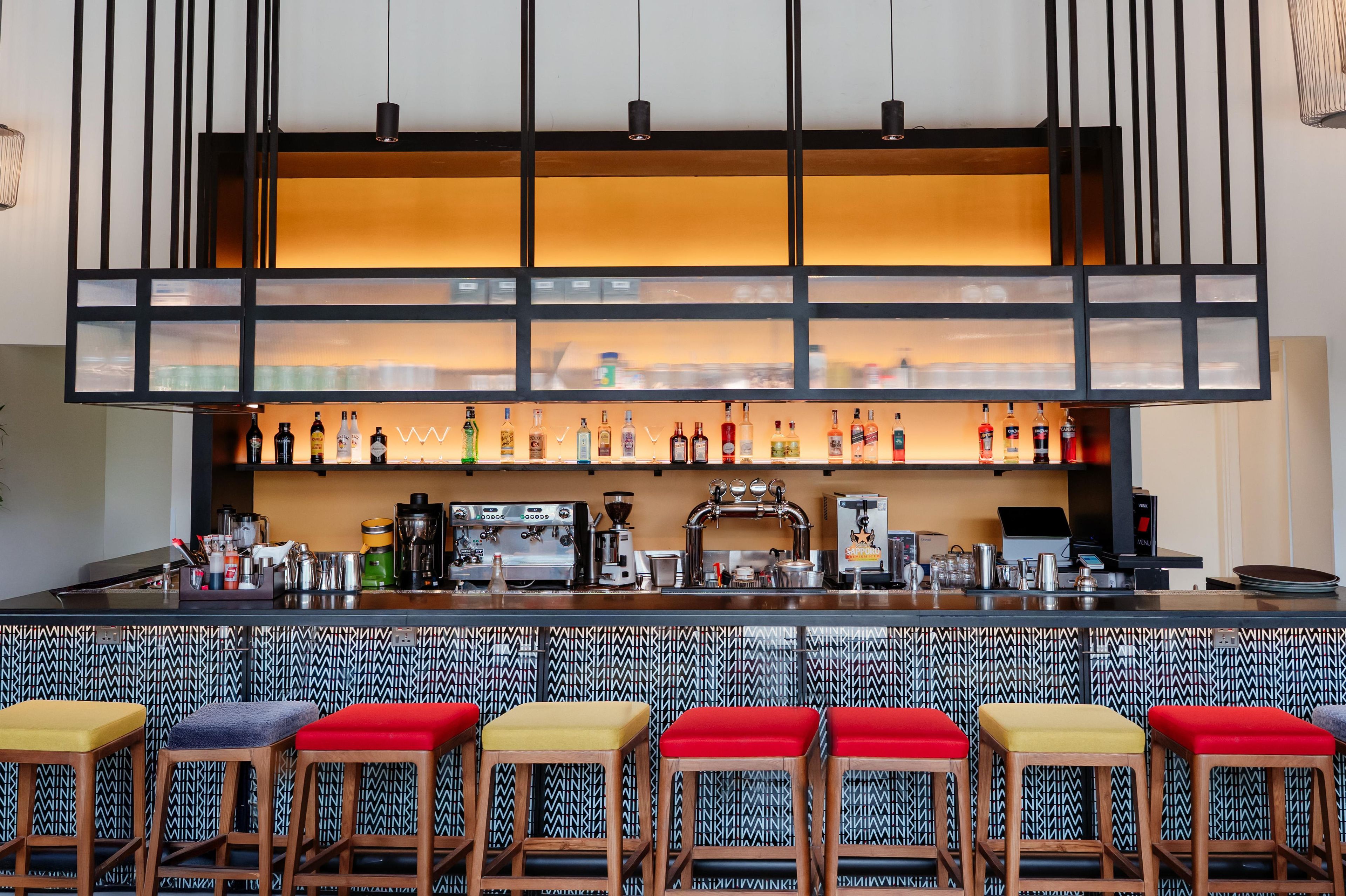 Una zona de bar con taburetes, una máquina de café y estantes con botellas.