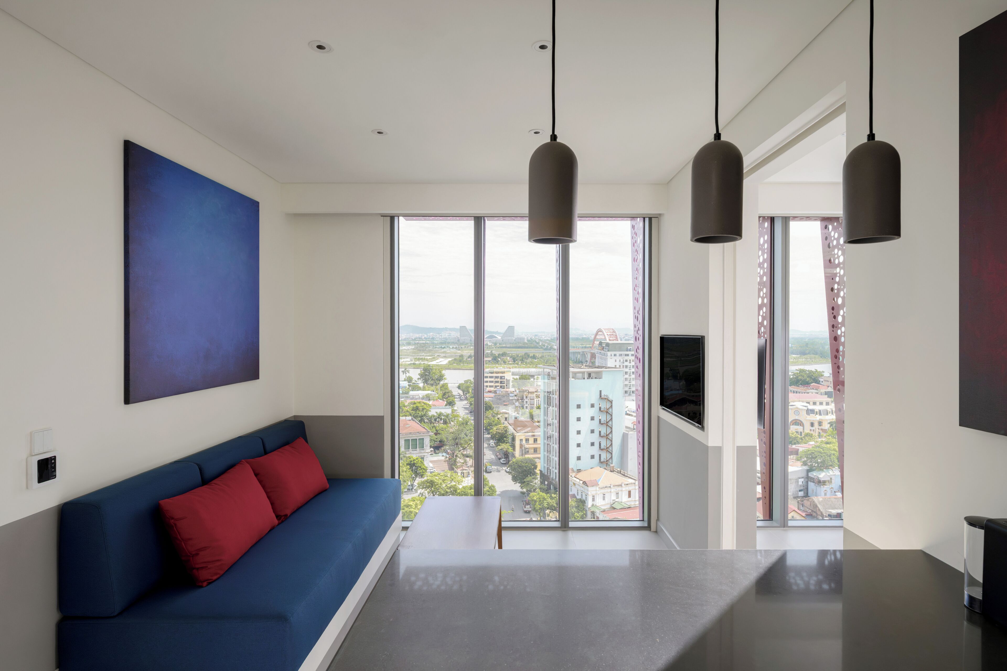 A modern living room with a blue sofa, a large window with a city view, and pendant lighting.