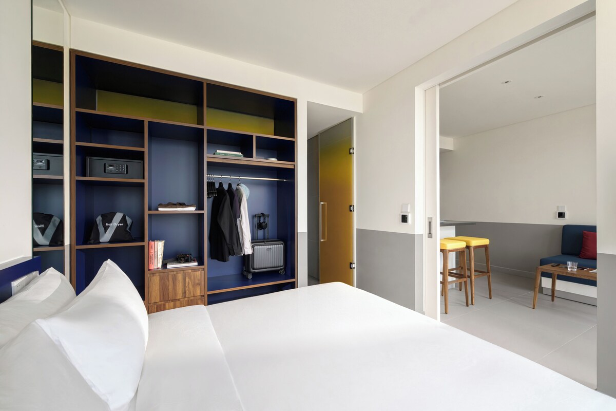 A modern hotel room with a large bed, a walk-in closet, and a small kitchenette area.