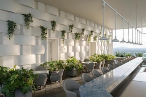 Un espace bar moderne avec des murs blancs, des plantes suspendues, des chaises en osier et un long comptoir.
