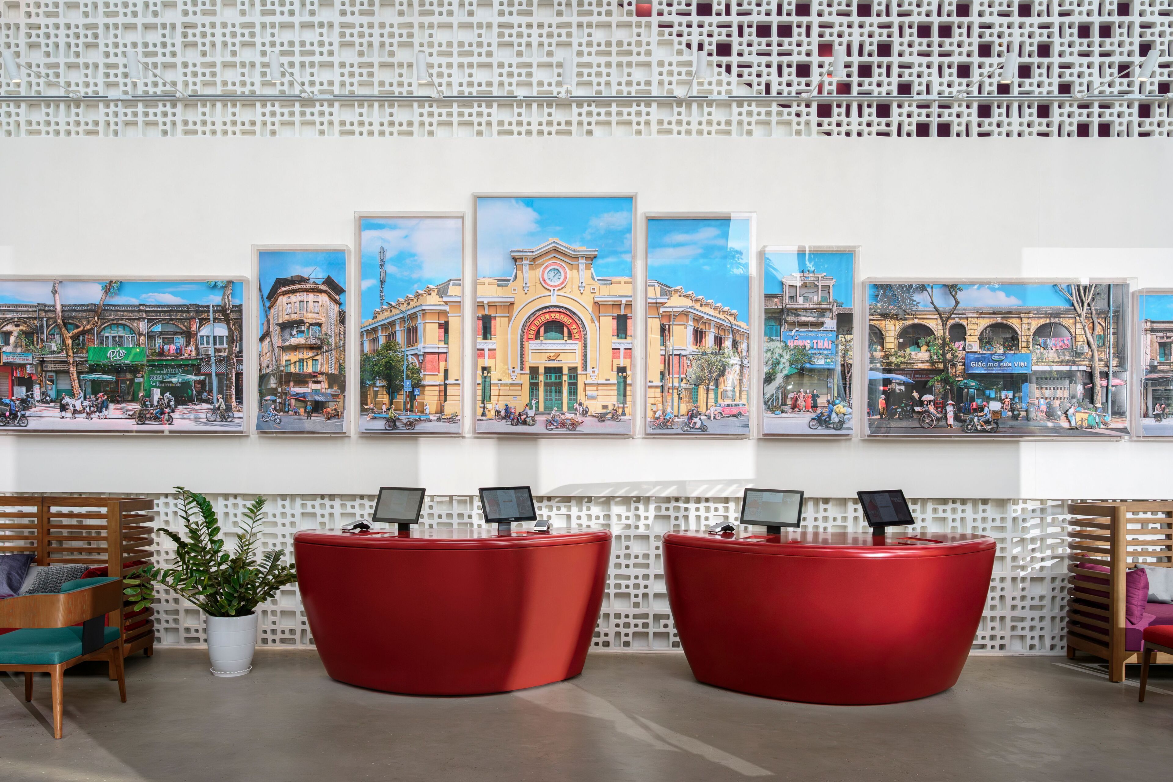 A reception area with a row of framed cityscape paintings, two red reception desks, and a potted plant.