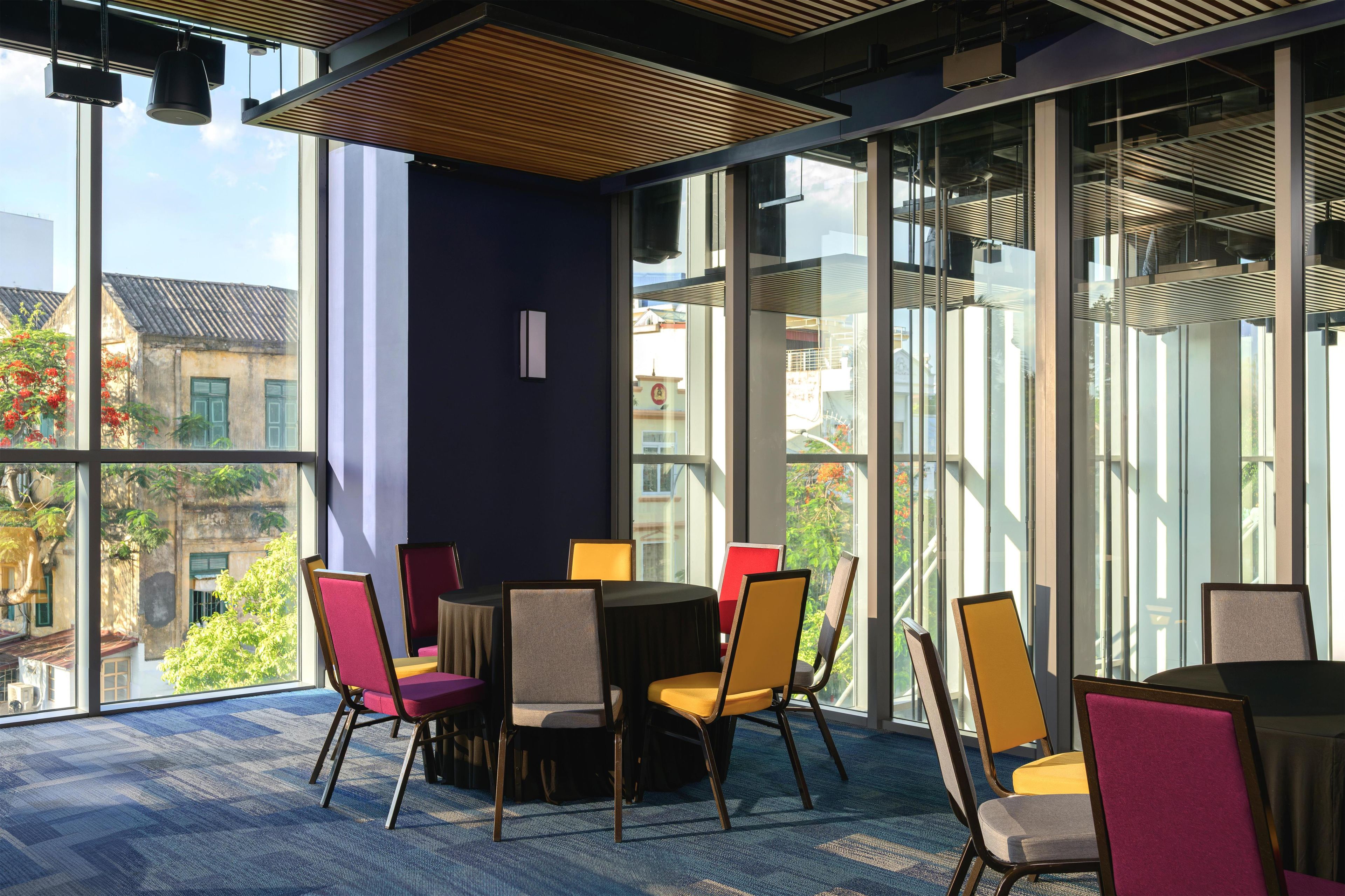 A modern indoor space with a round table and chairs, large windows, and a view of buildings outside.