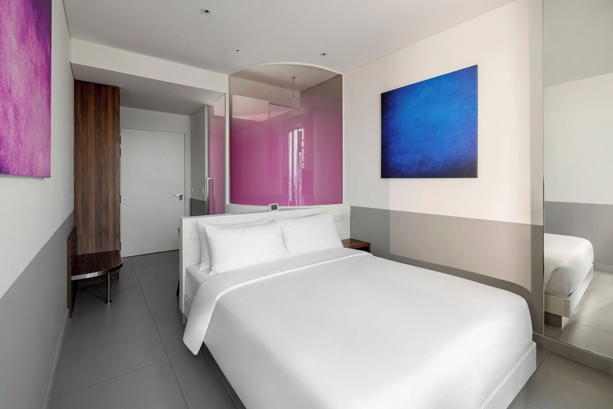 Une chambre d’hôtel moderne avec un grand lit, une table de chevet, une chaise et un tableau au mur.