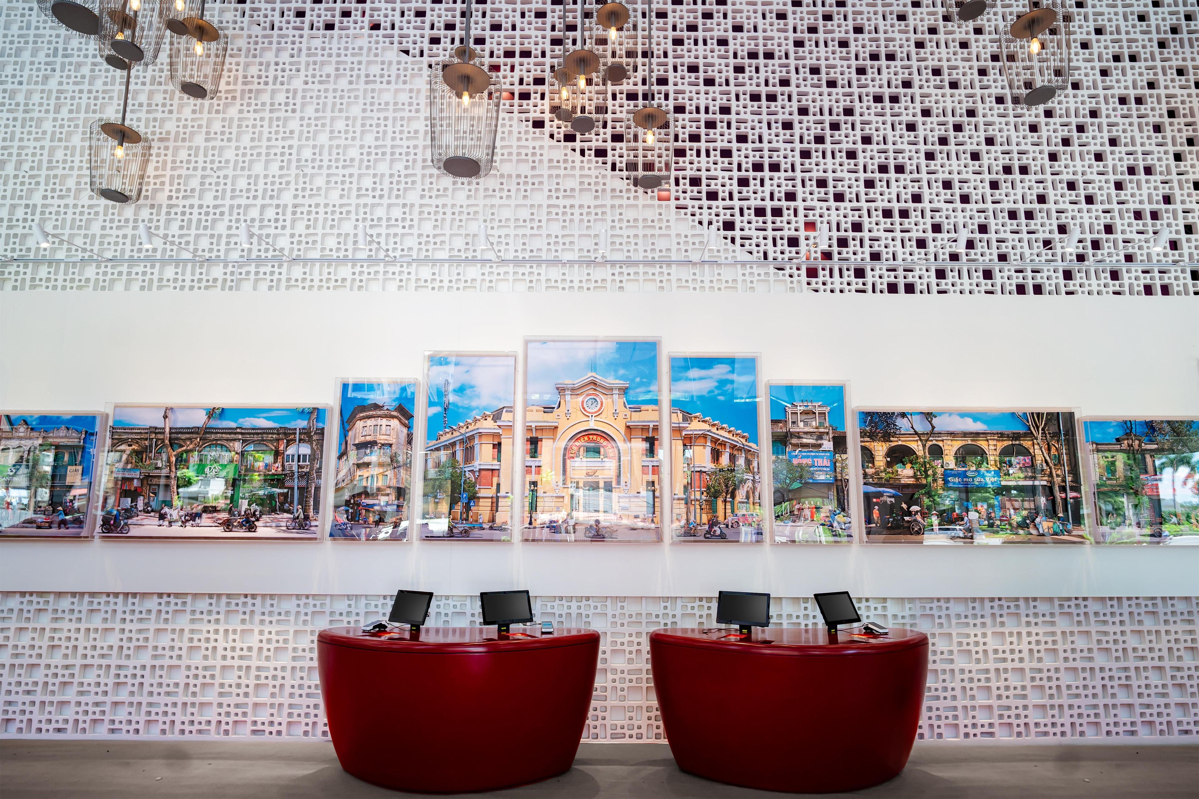 Un área de recepción con una pared decorada, varias obras de arte enmarcadas y dos zonas de estar rojas.