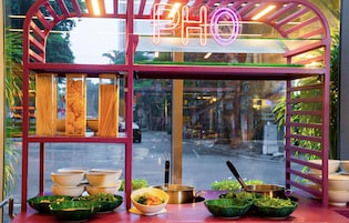 A food stall with a neon sign, bowls of food, and cooking utensils.