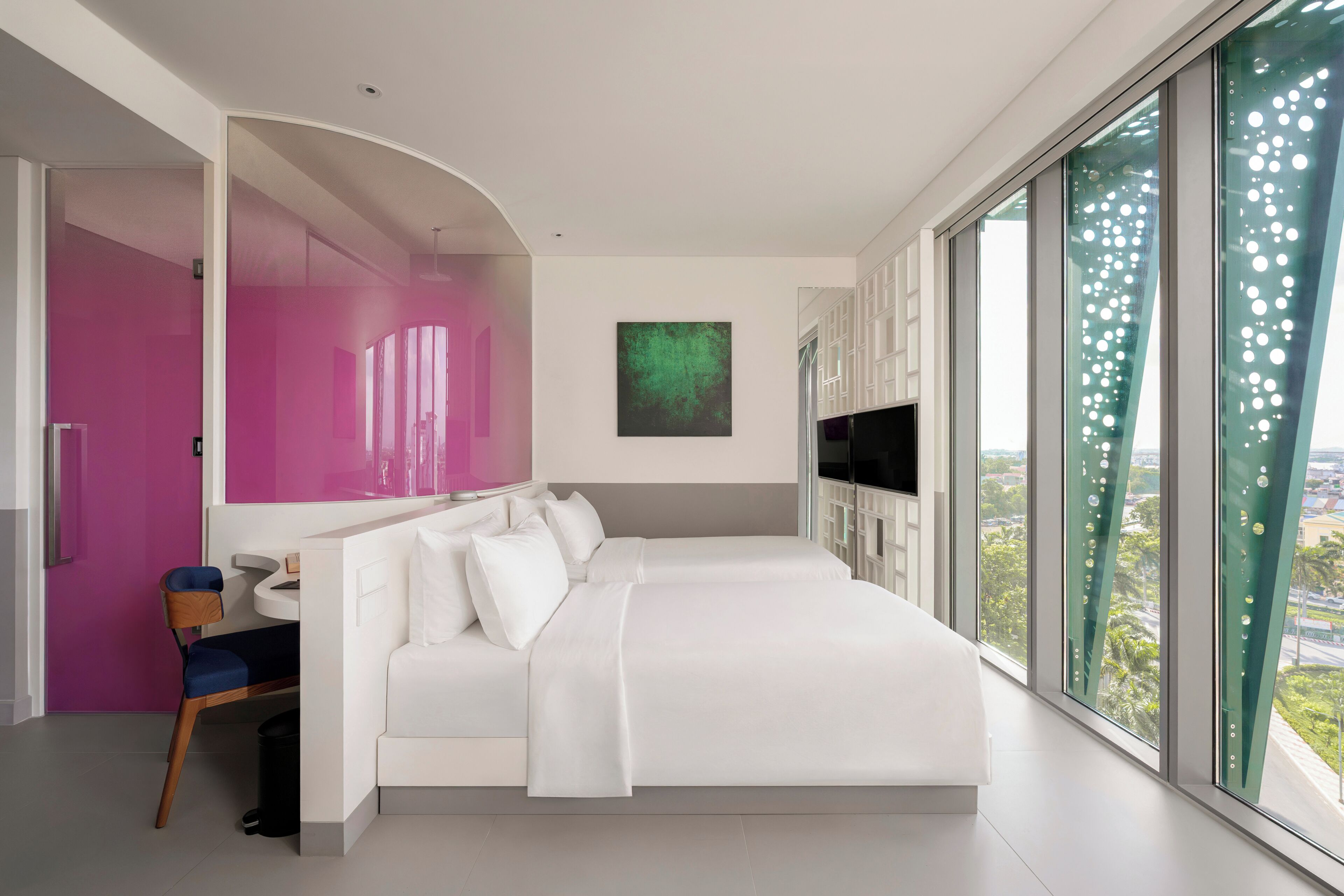 Un dormitorio moderno con una cama grande, un escritorio y vistas de la ciudad a través de ventanales de gran altura.