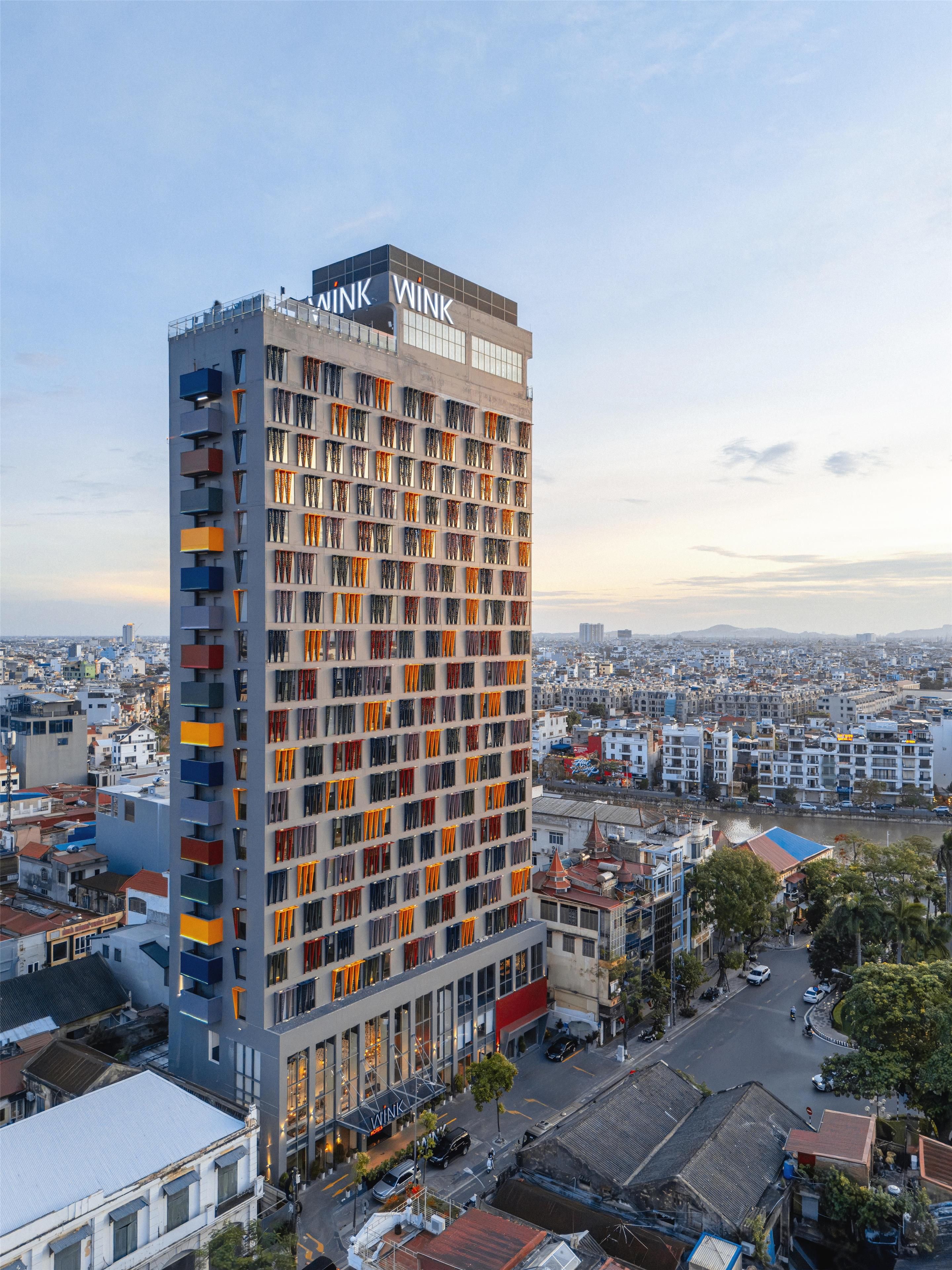 A high-rise building with a prominent 'WINK' sign, multiple balconies, and a view of the surrounding cityscape.