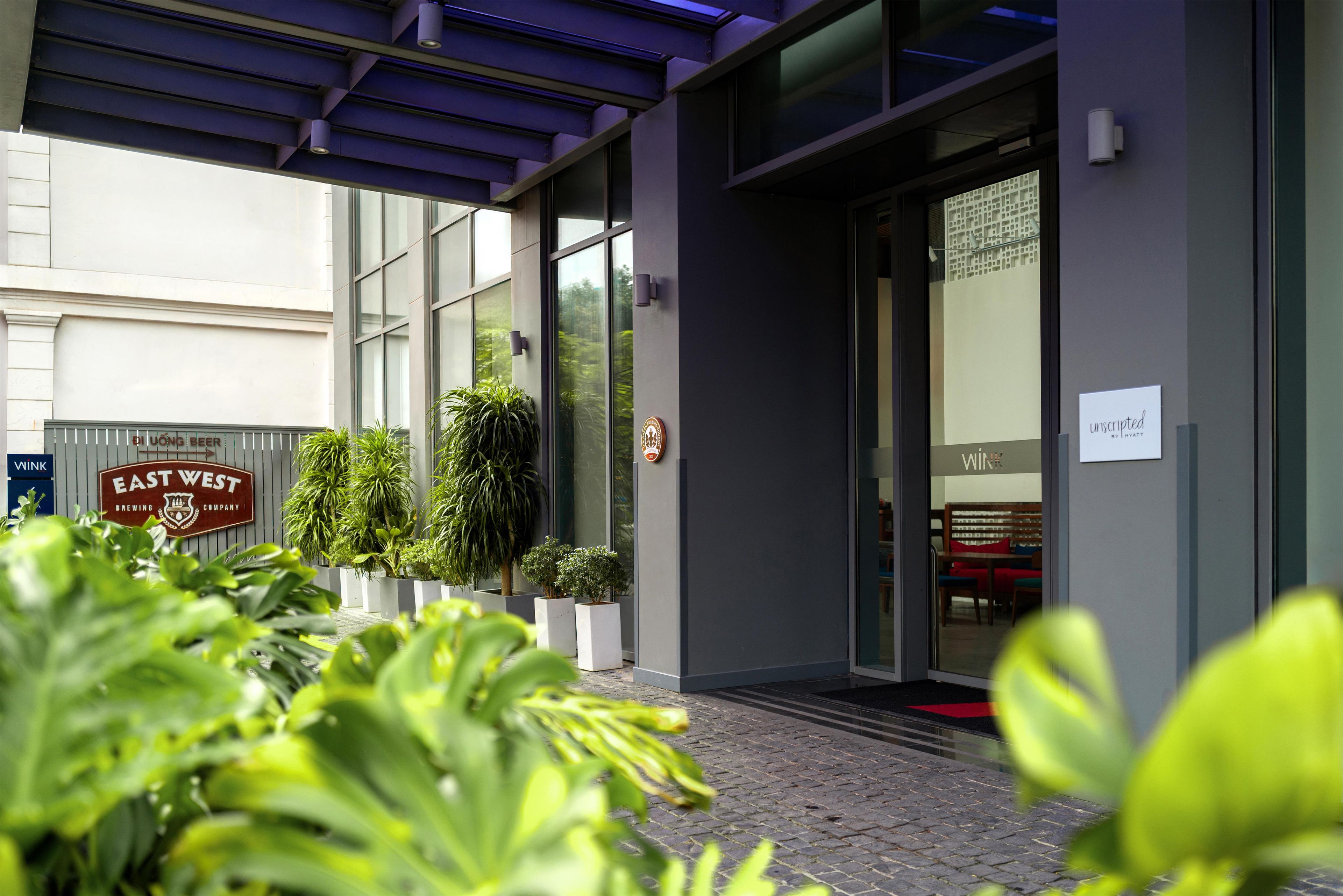 Ein Hotel Eingang mit modernem Design, inklusive Glastür, Topfpflanzen und einem Schild für 'East West Brewing Company'.