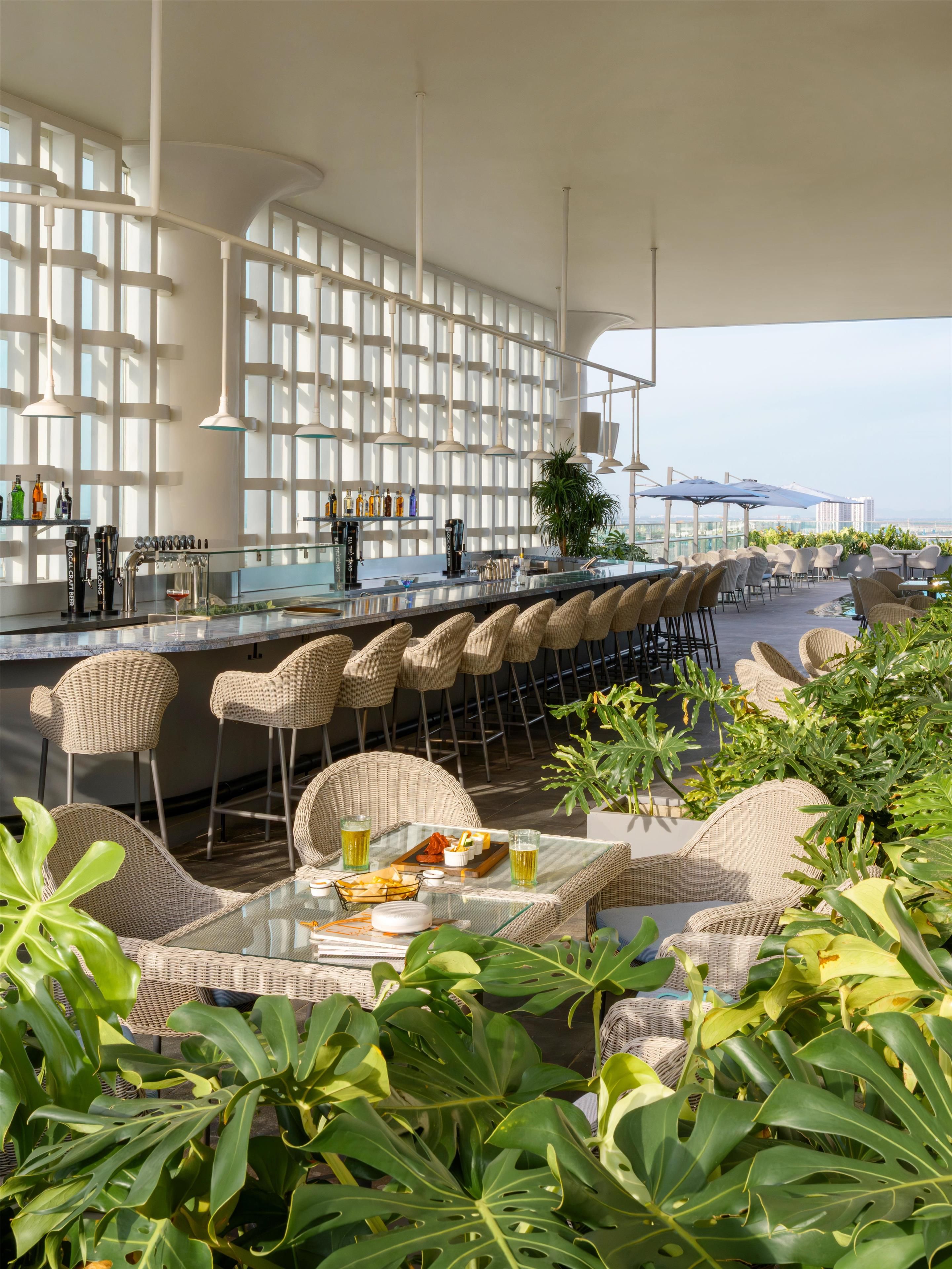 A bar area with a long counter, wicker chairs, and a view of the sea.