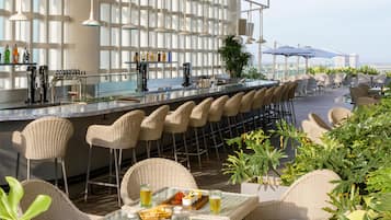 A bar area with a long counter, wicker chairs, and a view of the sea.