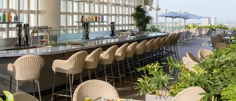 A bar area with a long counter, wicker chairs, and a view of the sea.
