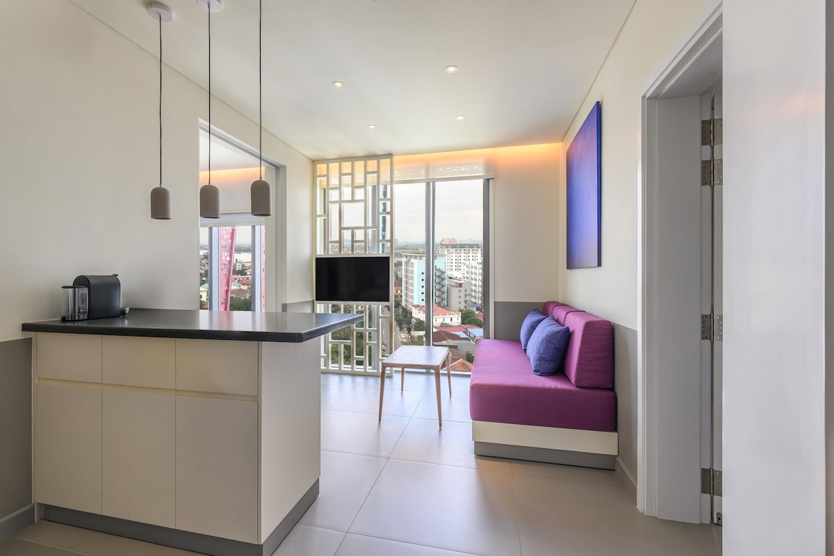 Un appartement moderne comprenant une cuisine, un coin repas, un salon avec un canapé et une grande fenêtre offrant une vue sur la ville.
