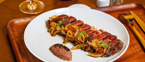 A plate of steak with onions, a glass of red wine, and a bottle of wine on a wooden table.