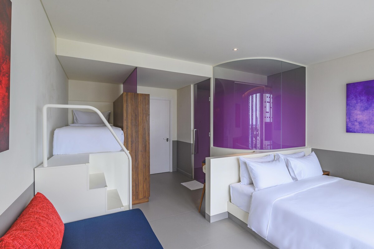Een moderne hotelkamer met een bed, een slaapbank, een bureau en een badkamer.