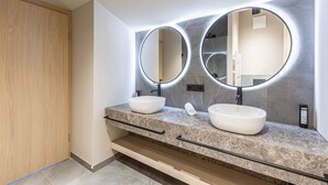 Une salle de bain moderne avec deux miroirs ronds, une porte en bois et un plan de toilette en marbre.