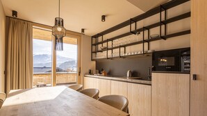 Une cuisine moderne avec une table et des chaises en bois, un four encastré et une vue sur les montagnes grâce à de grandes fenêtres.
