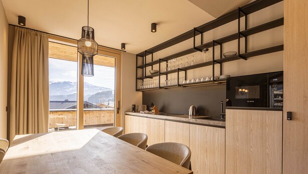 Eine moderne Küche mit Holztisch und -stühlen, einem eingebauten Backofen und Bergblick durch große Fenster.