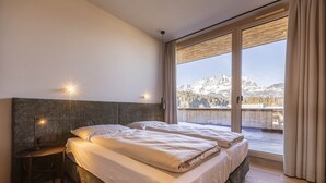 Une chambre avec deux lits, une table de chevet, une lampe et une grande fenêtre donnant sur la montagne.