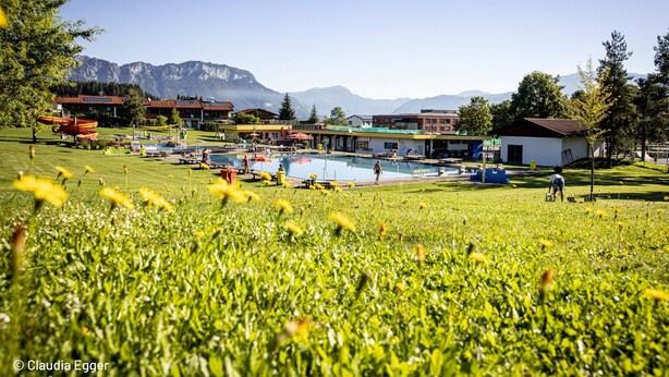 Un hôtel doté d’une piscine, entouré d’une pelouse et avec des montagnes en toile de fond.