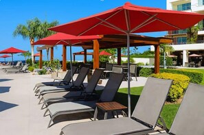 Un espace aménagé au bord de la piscine, avec des chaises longues et des parasols rouges.