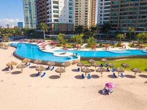 A resort with a large swimming pool, sun loungers, and thatched umbrellas.