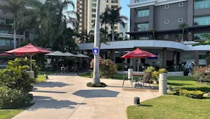 Un patio al aire libre con sombrillas rojas, asientos y un sendero que conduce a la entrada de un edificio.