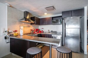 Une cuisine moderne avec des meubles de couleur sombre, des appareils électroménagers en acier inoxydable et un plan de travail en granit.