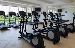 A gym with multiple treadmills arranged in rows, large windows, and a tiled floor.