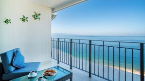 A balcony with a view of the sea, a glass table with a croissant, and a blue sofa.