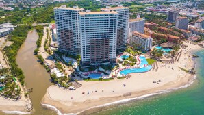 A high-rise hotel with multiple floors, a swimming pool, and a beach area.