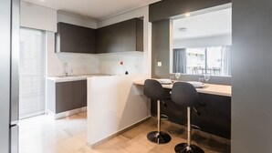 A modern kitchen with a central island, two bar stools, and a window overlooking the street. - Spacious and Sunlit Seaside Flat (Alimos)