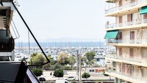 A view from a balcony overlooking a marina with boats, a white van, and a building with a green awning. - Spacious and Sunlit Seaside Flat (Alimos)