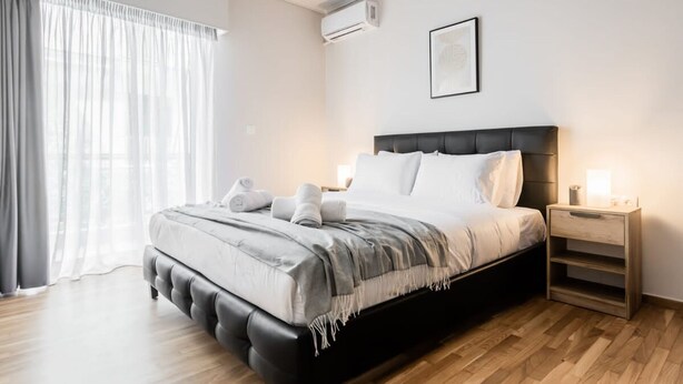 A modern bedroom with a large bed, wooden flooring, a nightstand, and a window with sheer curtains. - Spacious and Sunlit Seaside Flat (Alimos)
