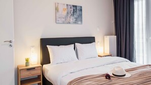 A hotel room with a bed, bedside tables, a wall-mounted artwork, and a window with curtains. - Spacious Seaside Flat at Alimos (Alimos)