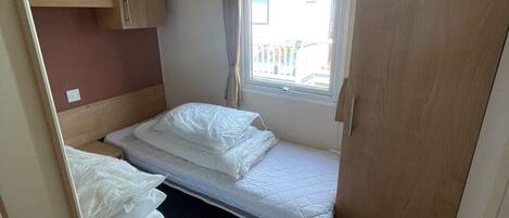 A compact room with two beds, a window with curtains, and a ceiling light.