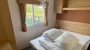Un lit simple avec une literie blanche, dans une pièce dotée d’une fenêtre, de rideaux et d’une tête de lit en bois.