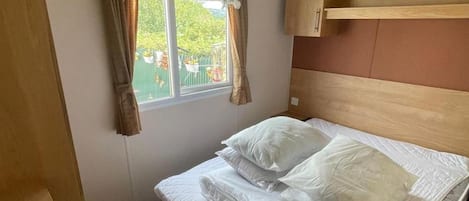 Un letto singolo con biancheria da letto bianca in una stanza con finestra, tende e una testiera in legno.