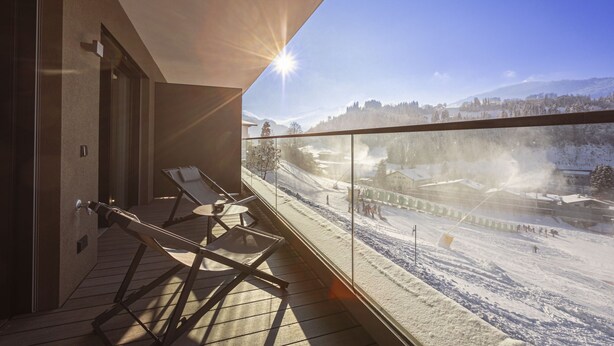 A balcony with sun lounger chairs, a glass railing, and a view of a snowy ski slope.