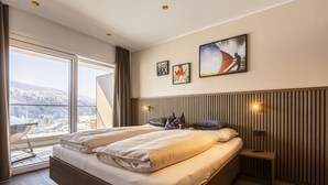 A modern hotel room with a large bed, a view of a snowy landscape, and a wooden headboard.