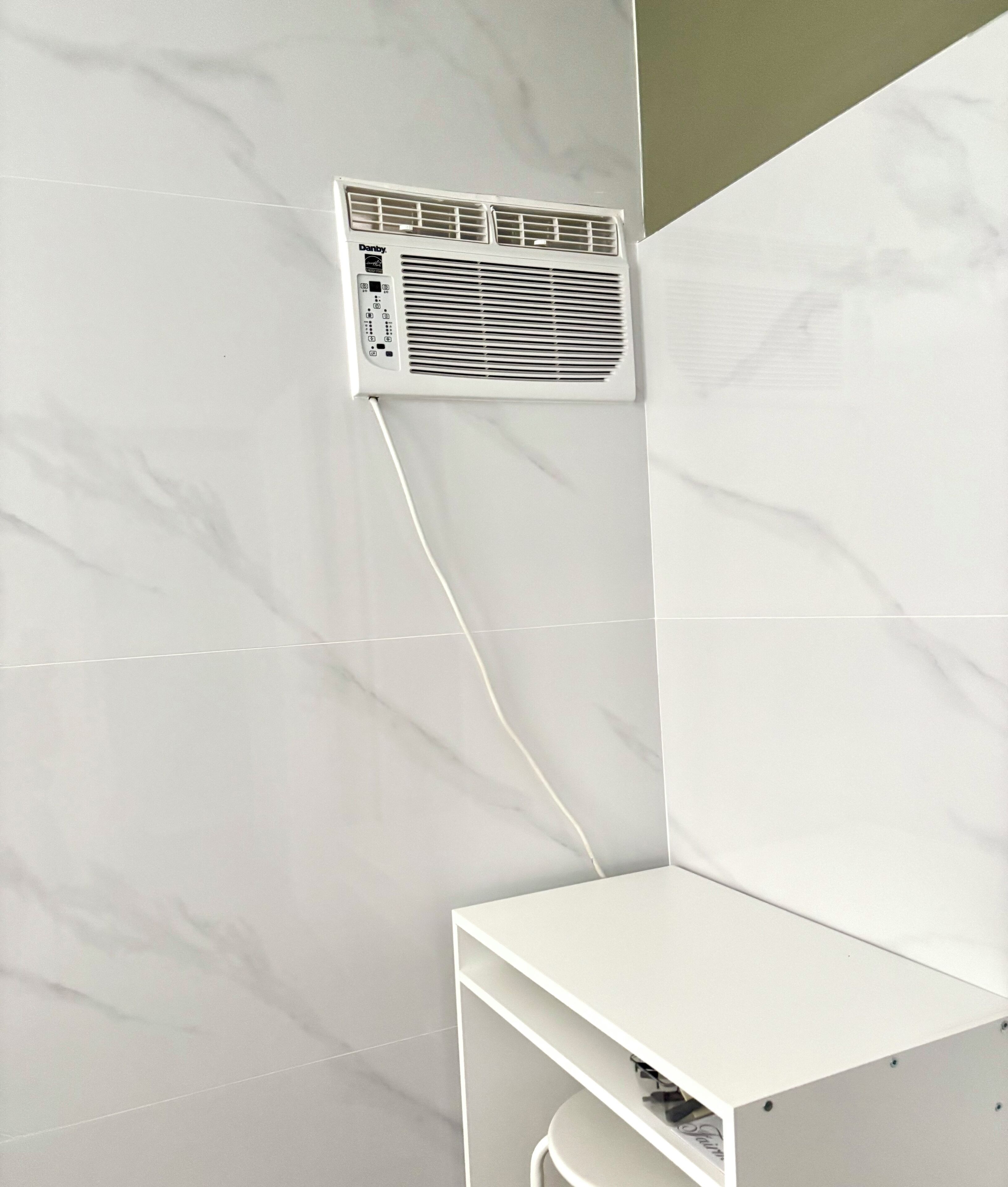 Une salle de bain avec un mur en marbre blanc, une étagère blanche et un appareil de climatisation blanc fixé au mur.