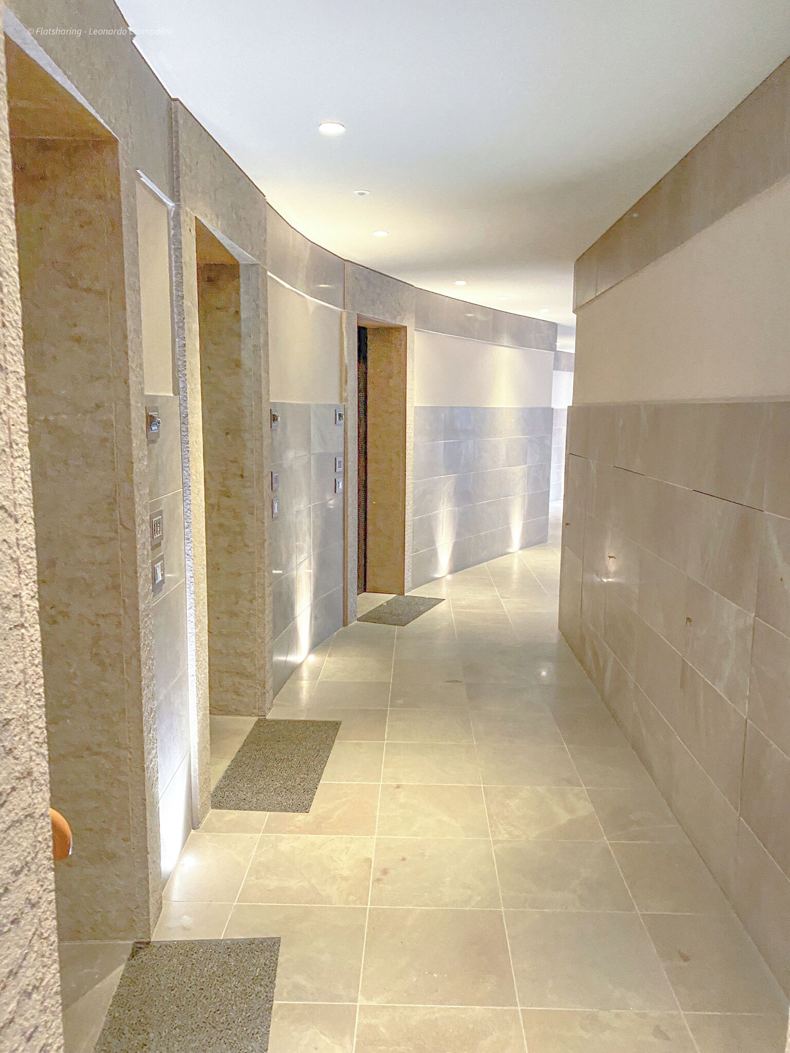 Een moderne gang met een gebogen plafond, inbouwverlichting en een combinatie van gestructureerde en gladde wanden.