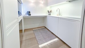 Une cuisine moderne avec des armoires blanches, un four encastré, une machine à café et un évier avec un robinet.
