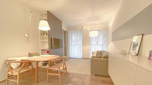 Un salon moderne avec une table à manger en bois, deux chaises, un canapé et un téléviseur fixé au mur.