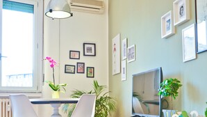 Een moderne woonkamer met een eethoek, een televisie op een witte kast, en verschillende foto’s in lijsten aan de muur.